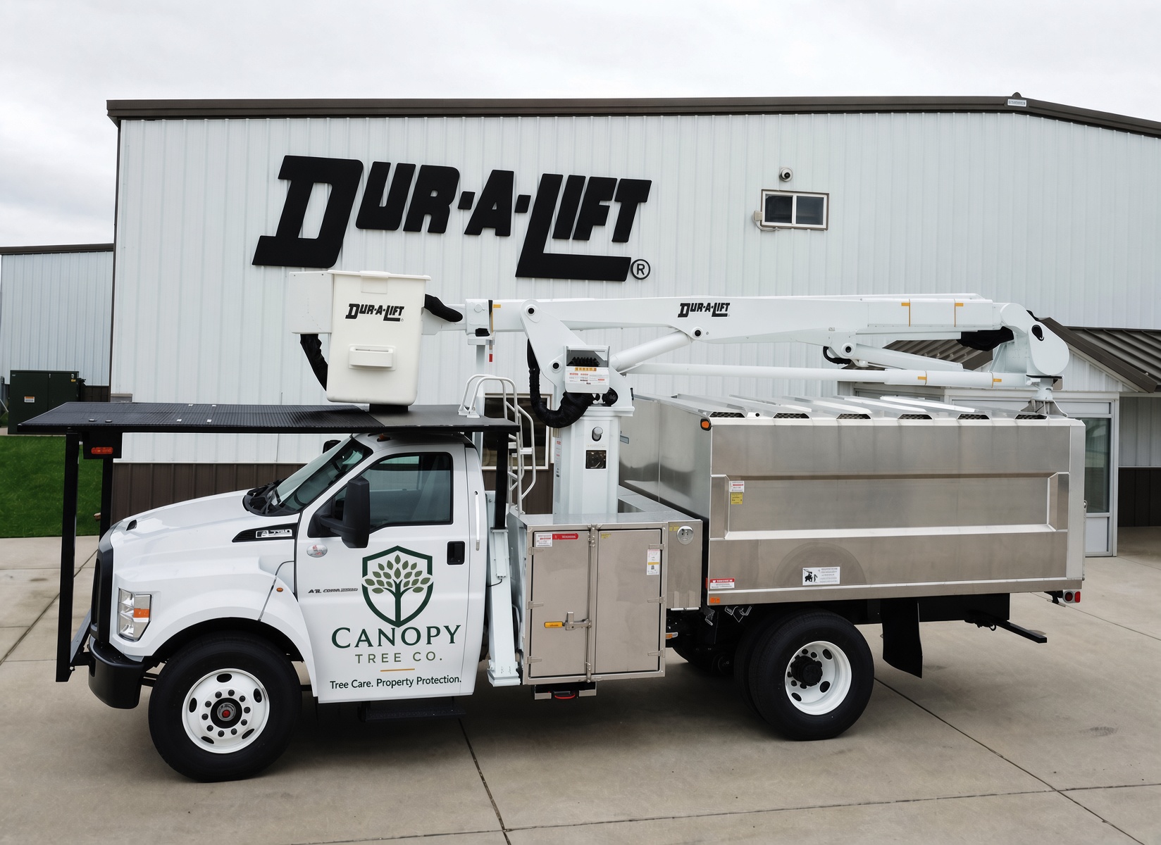 A Canopy Tree Co. white service truck with an aerial lift and chip body, parked on a concrete lot.